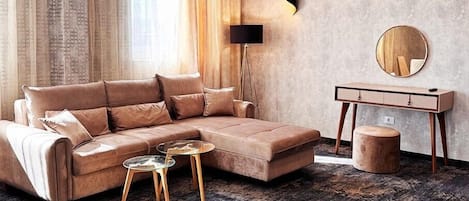 A modern living room with a sectional sofa, a round coffee table, a side table, a floor lamp, a mirror, and a patterned rug.