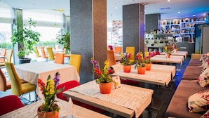 A restaurant with tables set for dining, potted plants, and a bar area with shelves of bottles. - AQUA Hotel (Varna)