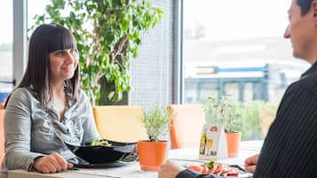 A dining table with a salad bowl, two potted plants, and a menu.