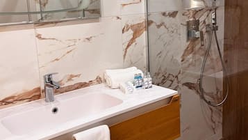 Un baño con lavamanos de mármol, tocador de madera, una toalla y artículos de aseo.