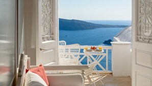 A balcony with white wicker furniture, a table with a plate of food and drinks, and a view of the sea and cliffs.