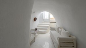 A minimalist white interior with a staircase leading to a window, a white sofa, and a small table with a chair.