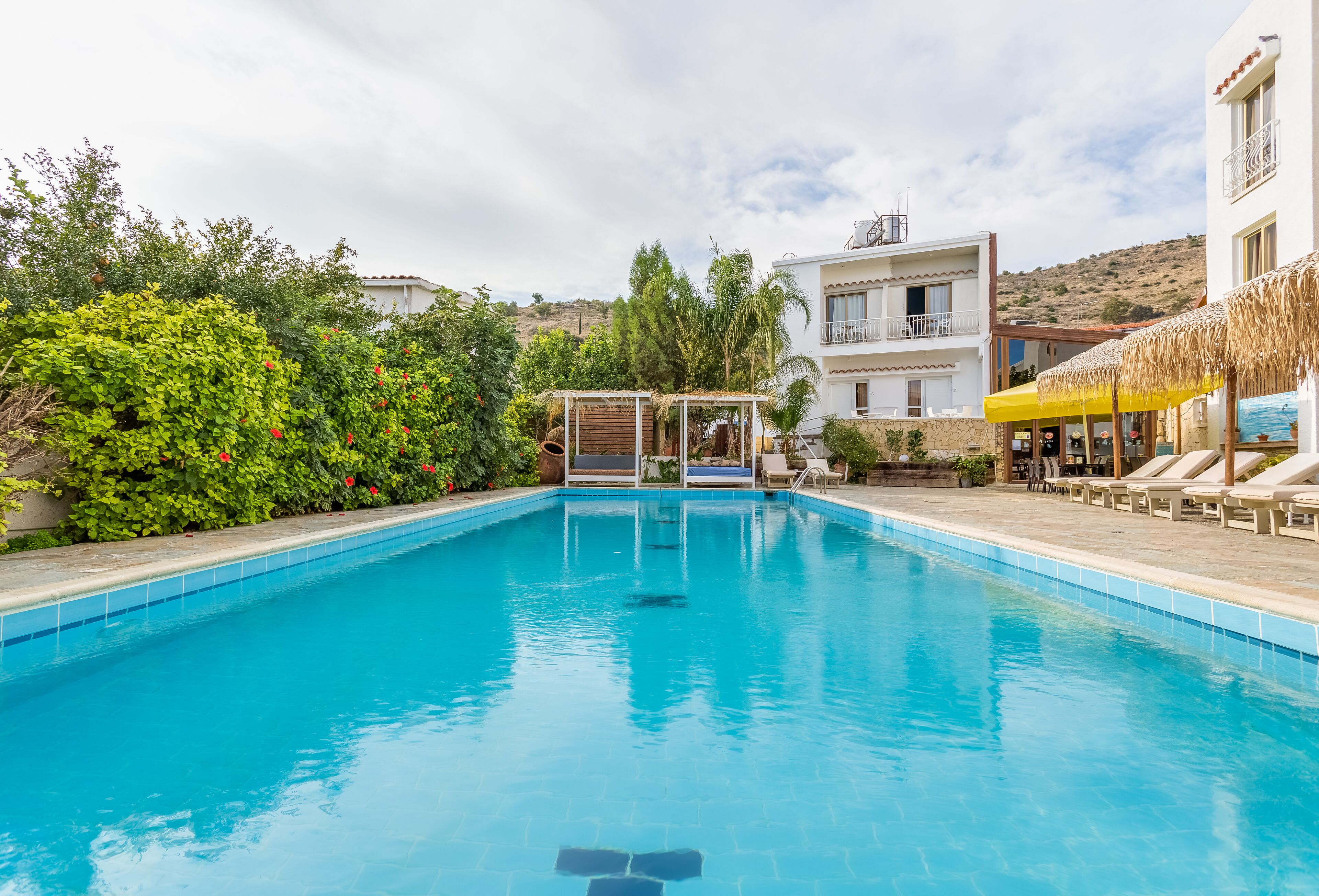Una piscina con solárium, rodeada de vegetación y un edificio con balcón.