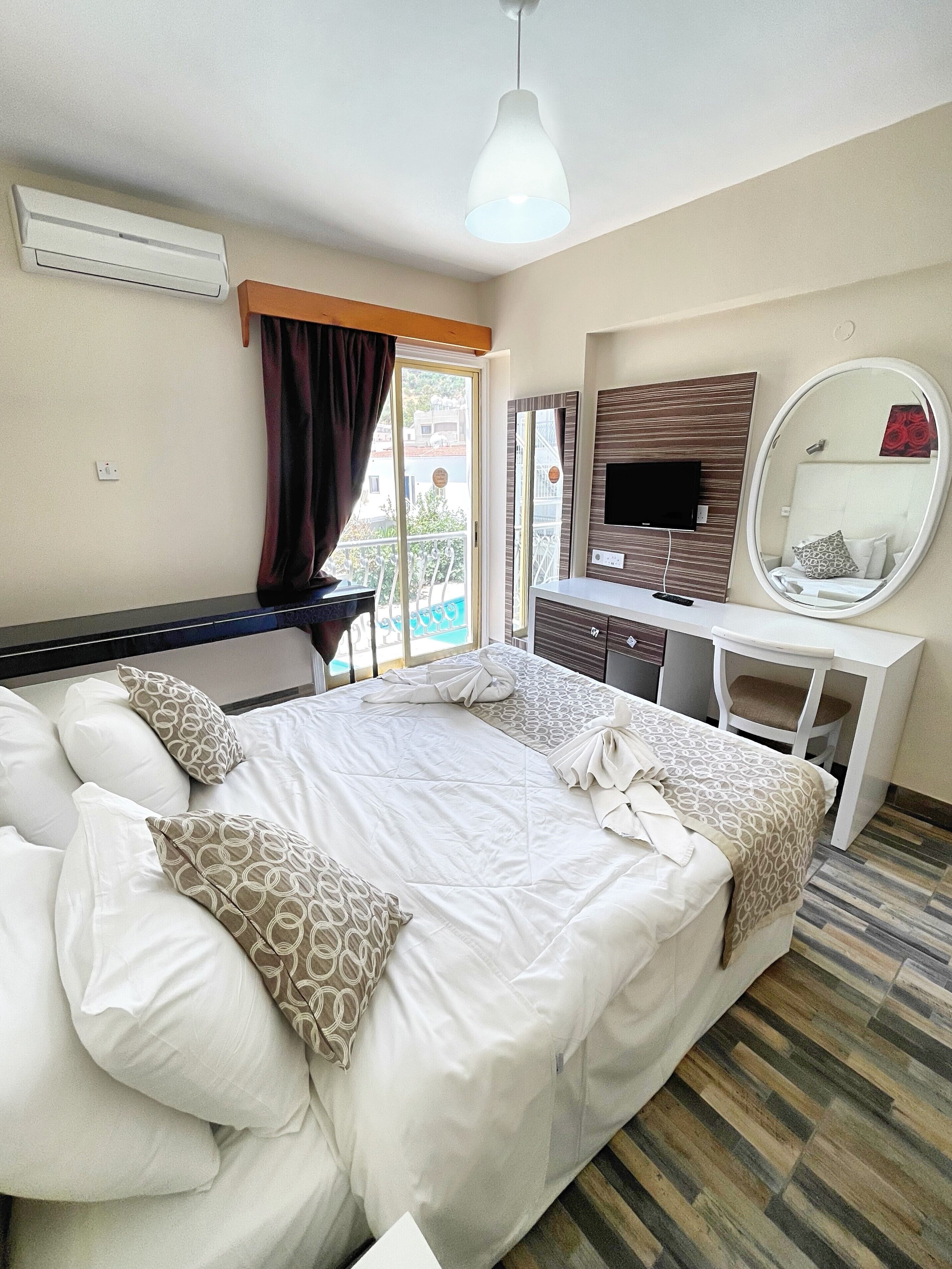 A hotel room with a large bed, a desk, a TV, and a balcony view.