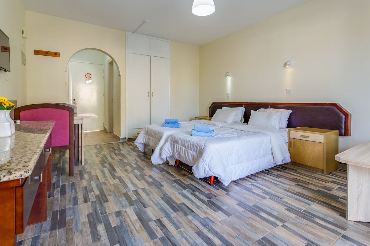 Quarto de hotel com cama, mesas de cabeceira, escrivaninha, cadeira e guarda-roupa.