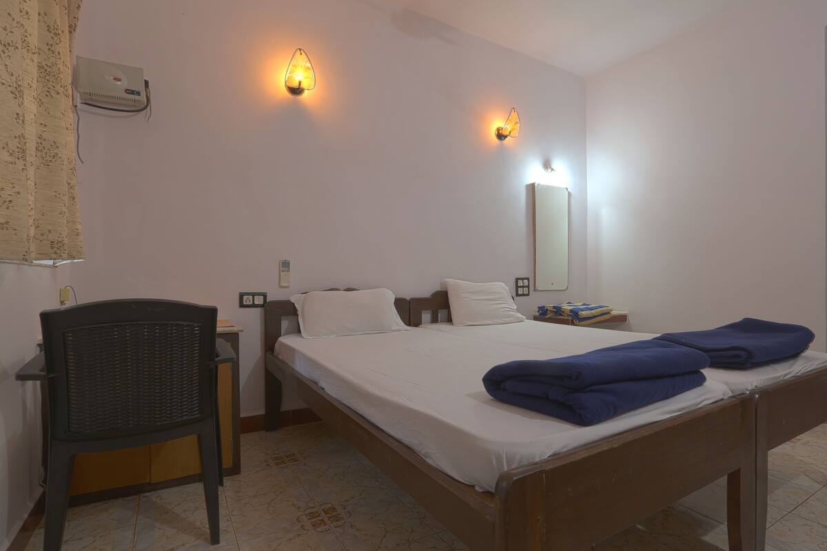 A hotel room with a single bed, a chair, a nightstand, and two wall-mounted light fixtures.