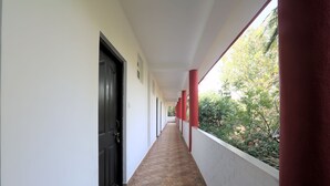 Un couloir au sol carrelé, aux murs blancs et aux piliers rouges.