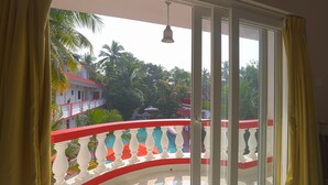 Un balcon doté d’une balustrade rouge et blanche, d’une porte-fenêtre coulissante et offrant une vue sur un immeuble avec un toit rouge et des palmiers.
