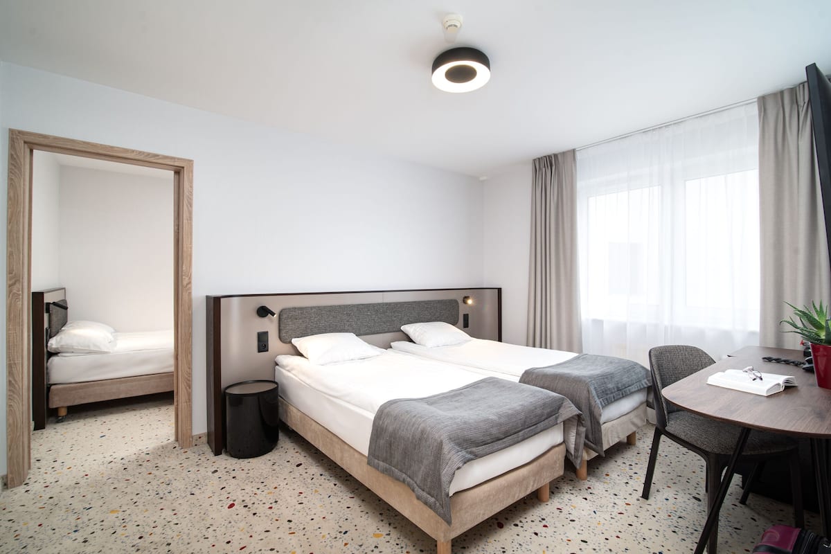 A hotel room with two beds, a round dining table, a chair, a mirror, and a ceiling light.
