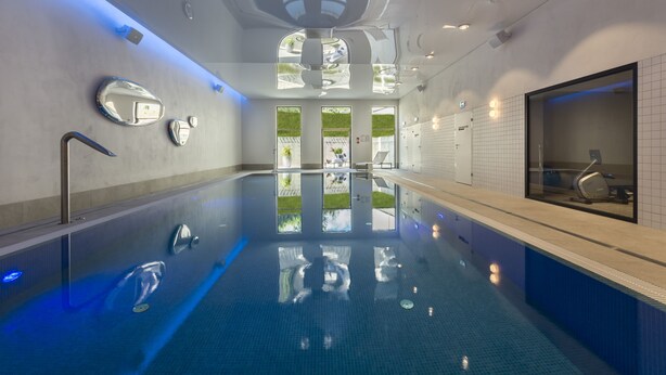 Una piscina interior con paredes de vidrio transparente, un techo con iluminación empotrada y vistas al exterior.