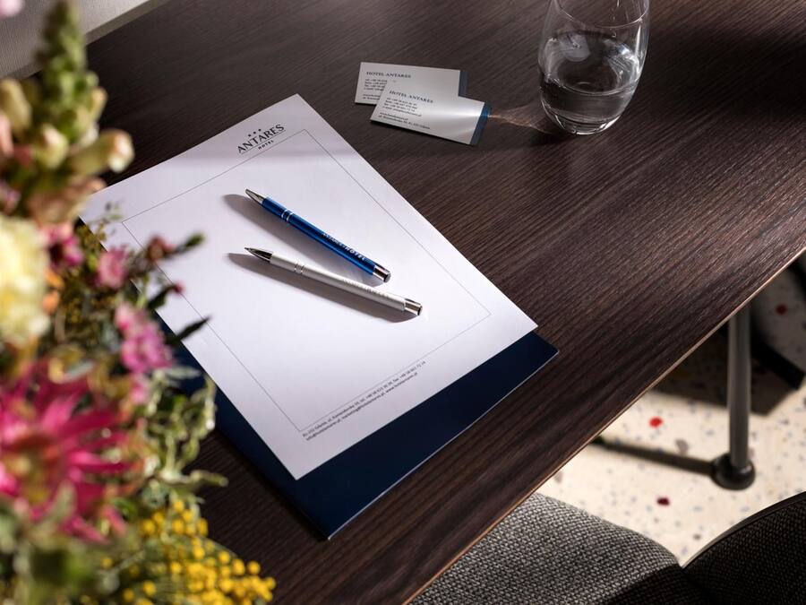 A hotel room with a wooden desk, a pen, a glass of water, and a business card.