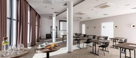A spacious hotel dining area with large windows, multiple tables, and chairs.