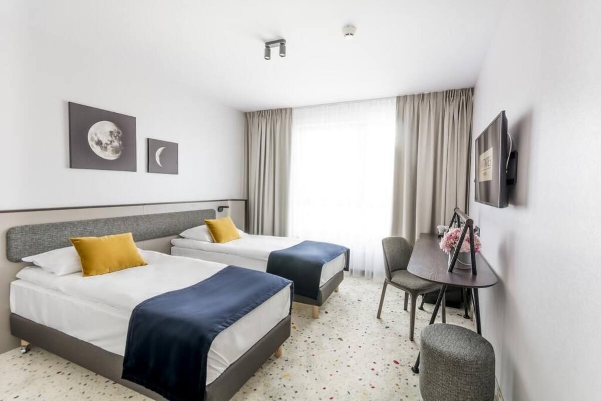 A hotel room with two beds, a small table, a chair, and a TV.