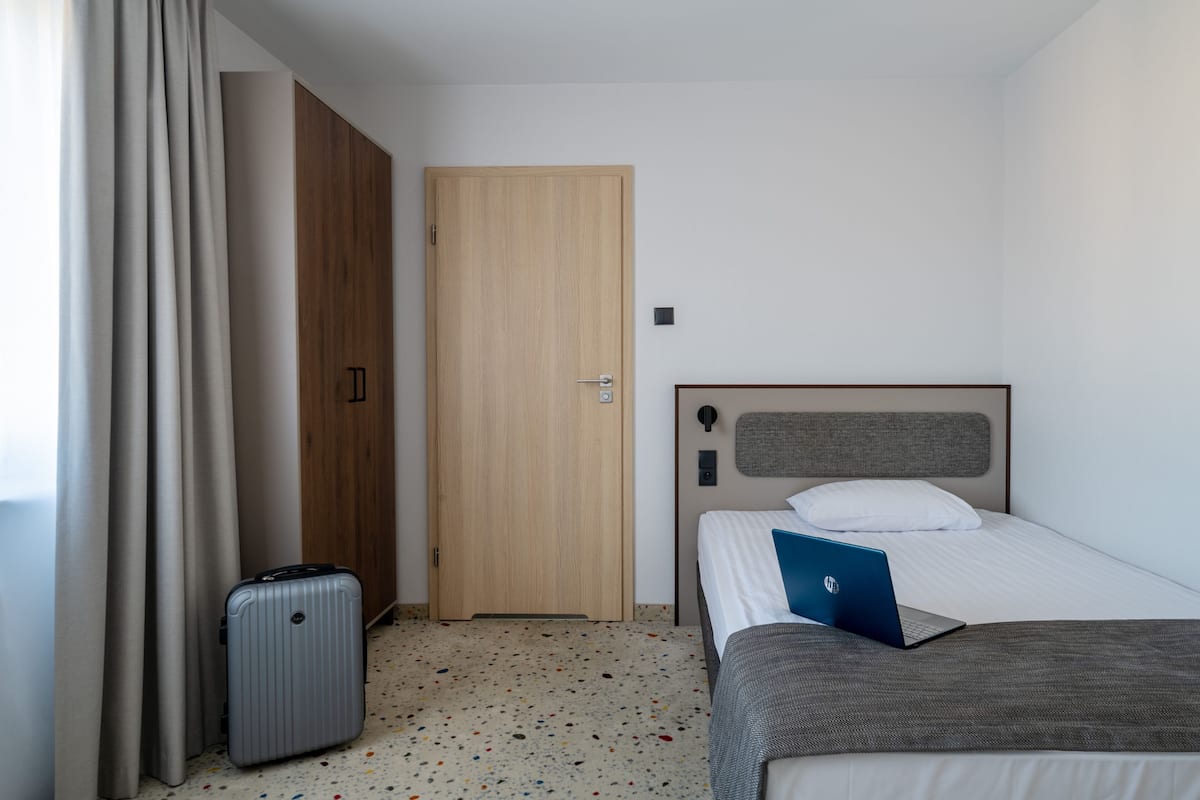 A hotel room with a bed, a desk with a laptop, a suitcase, and a wardrobe.