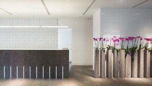 Een receptiebalie met een modern ontwerp, een muur met herhaalde tekst, en een rij betonnen plantenbakken met bloemen.