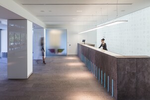 A modern reception area with a long counter, a large screen displaying a blurred image, and a person standing behind the counter.