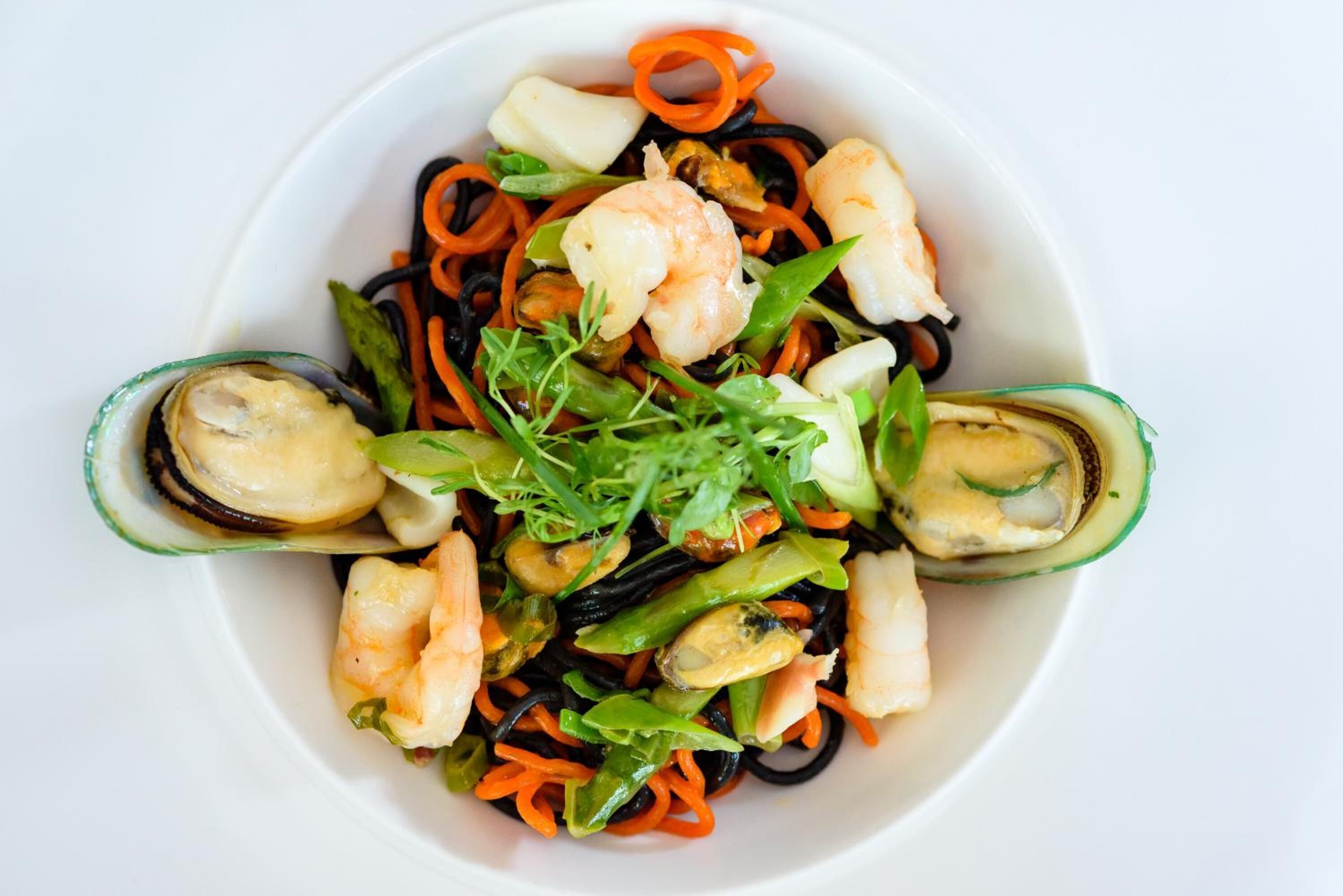 A bowl of seafood pasta with shrimp, mussels, and vegetables.