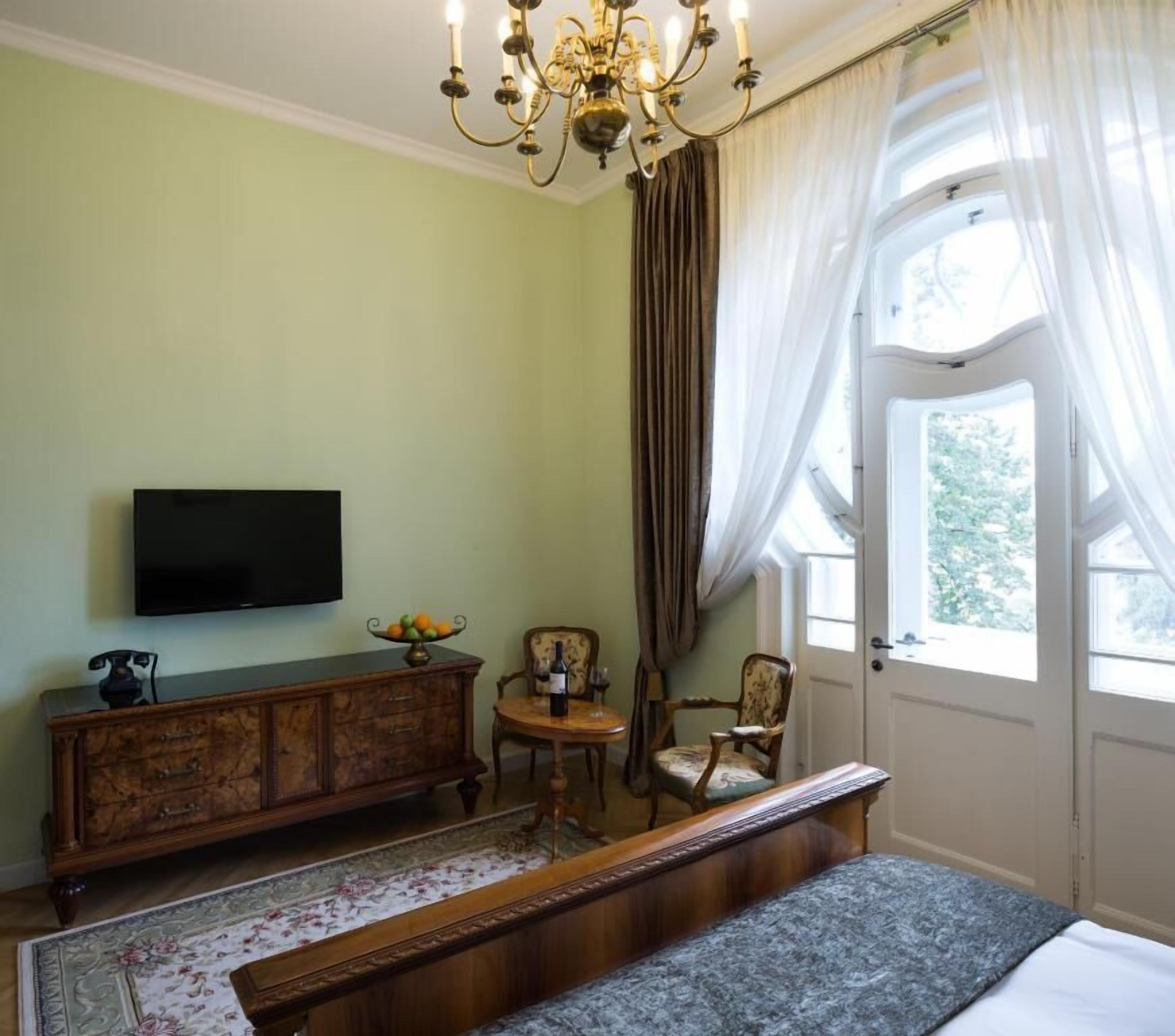 Een slaapkamer met een bed, een televisie, een houten dressoir, een stoel en een raam met gordijnen.