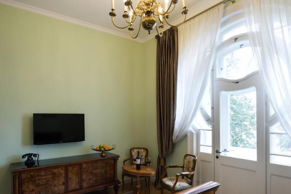 Une chambre à coucher comprenant un lit, un téléviseur, une commode en bois, une chaise et une fenêtre avec des rideaux.