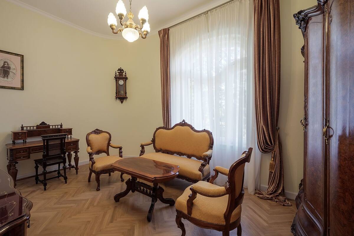 Een klassieke kamer met een houten zithoek, een eettafel, een klok en een kroonluchter.