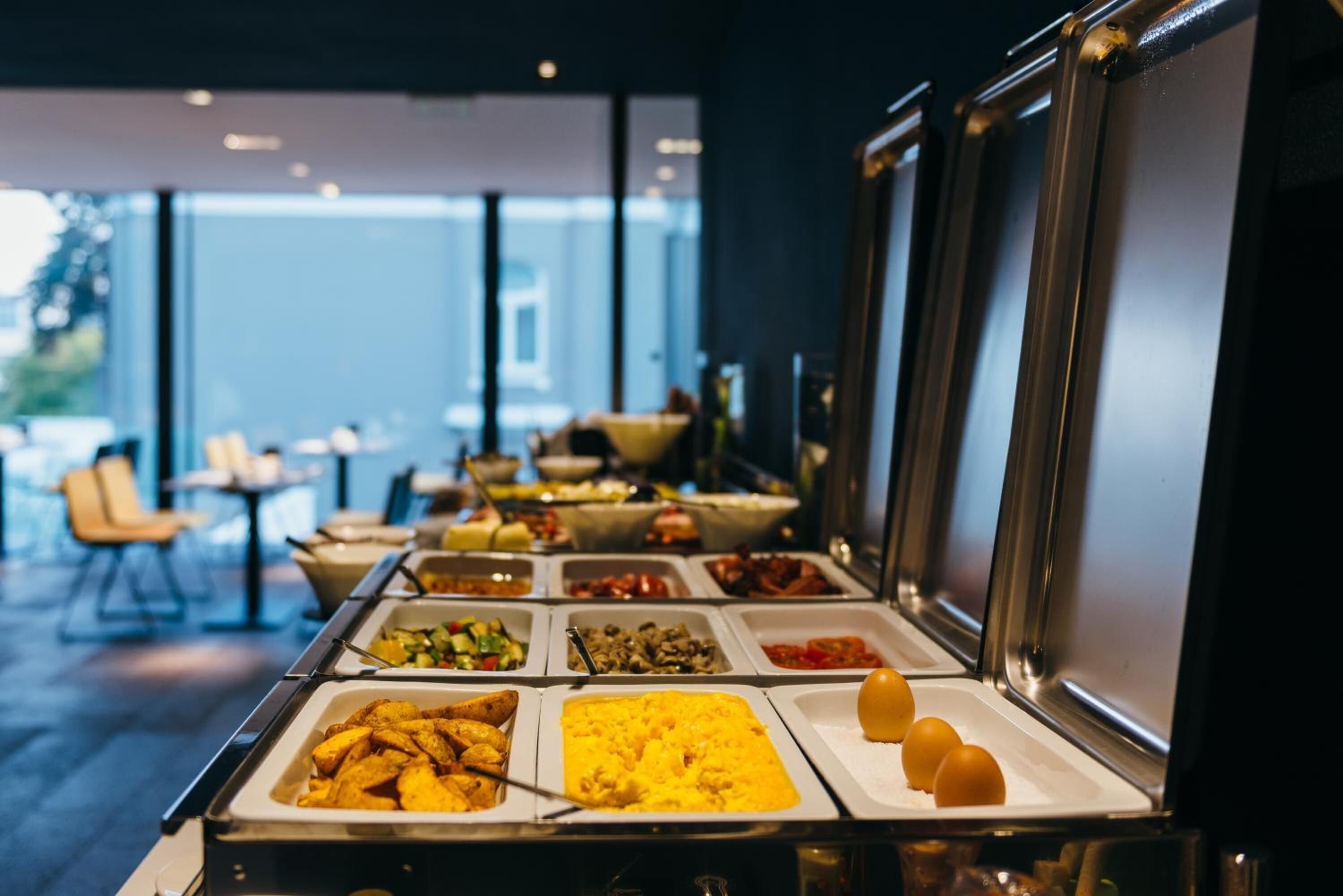 A buffet with various food options, including fried potatoes, scrambled eggs, and a selection of sauces.