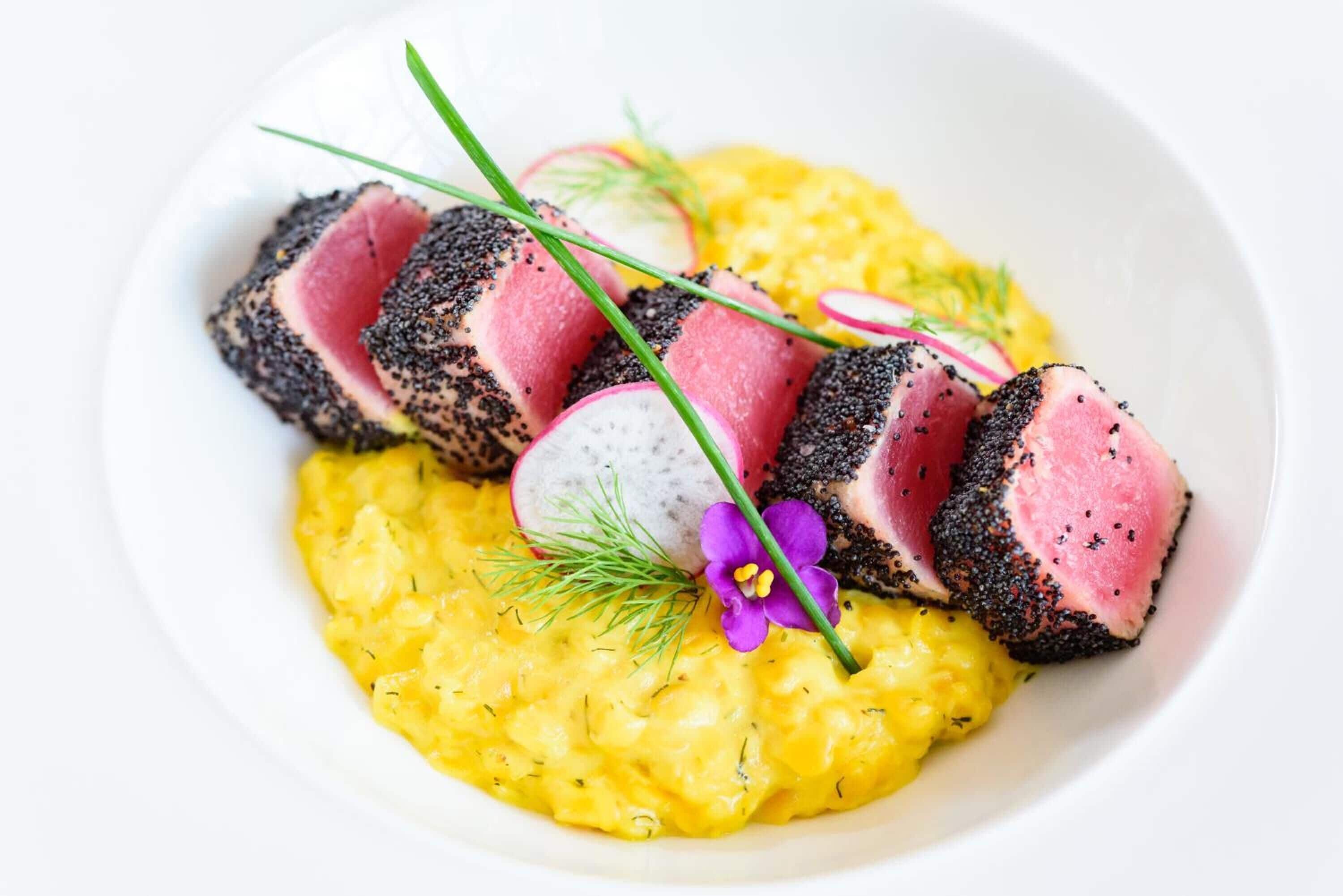Un plato con carne rosada, semillas negras y puré amarillo.