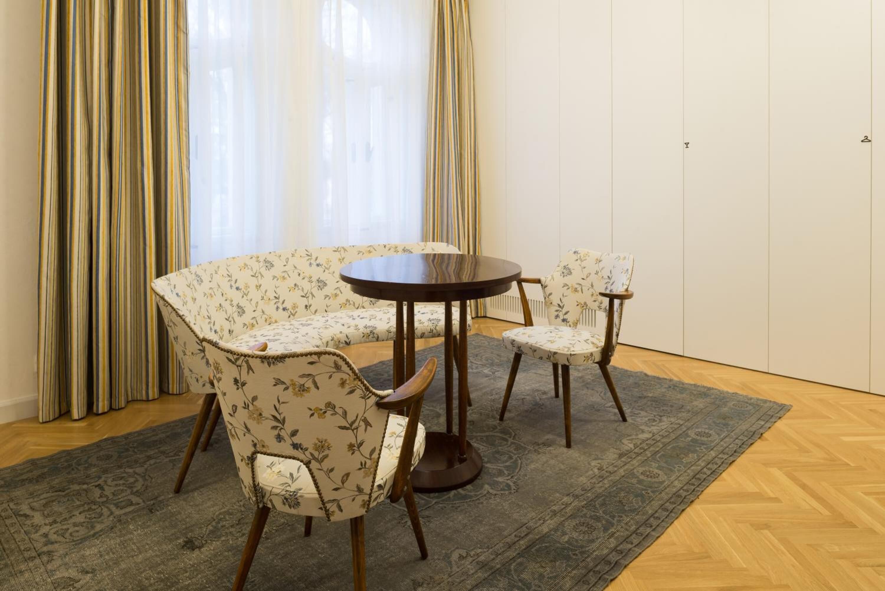 Ein Essbereich mit einem runden Tisch, zwei Stühlen, einem gemusterten Teppich und einem Fenster mit Vorhängen.