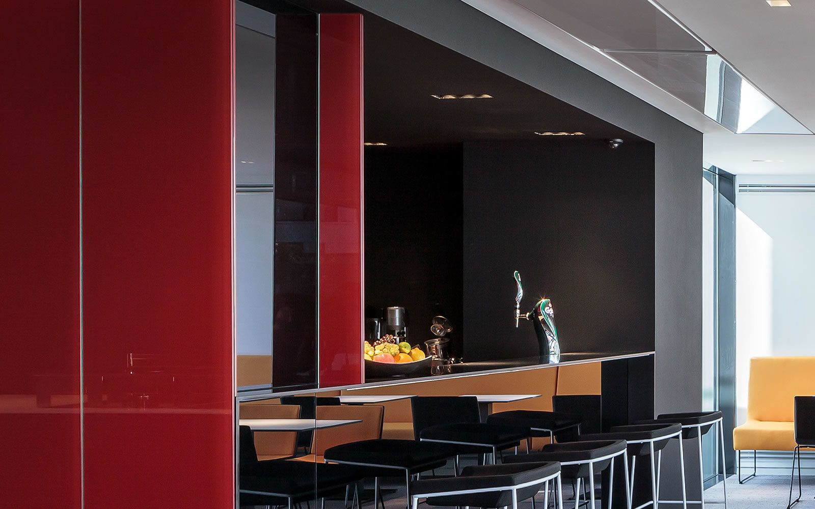A modern bar area with a long counter, black chairs, and a red accent wall.