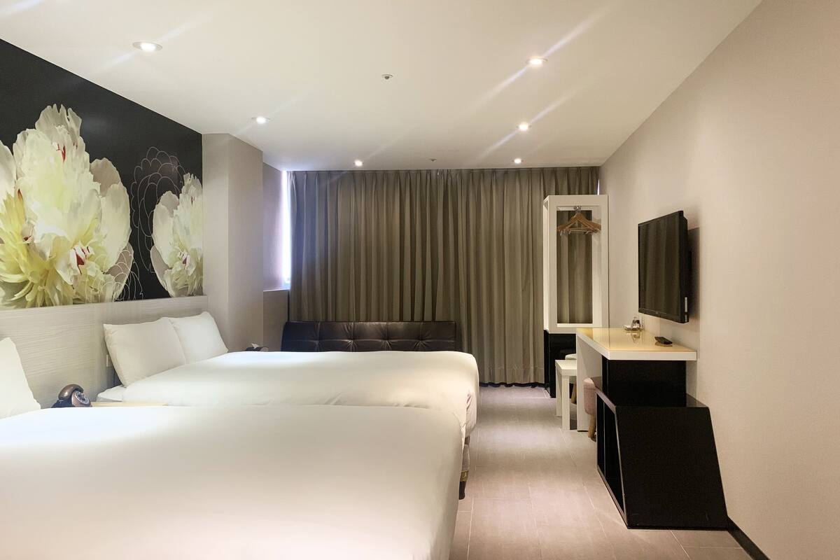 A hotel room with two beds, a large floral mural, a TV, and a desk with a mirror.