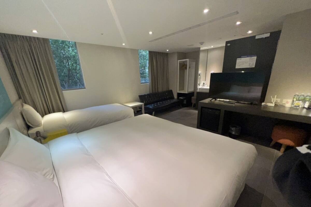 A hotel room with a large bed, a desk with a computer, a TV, and a seating area with a couch.