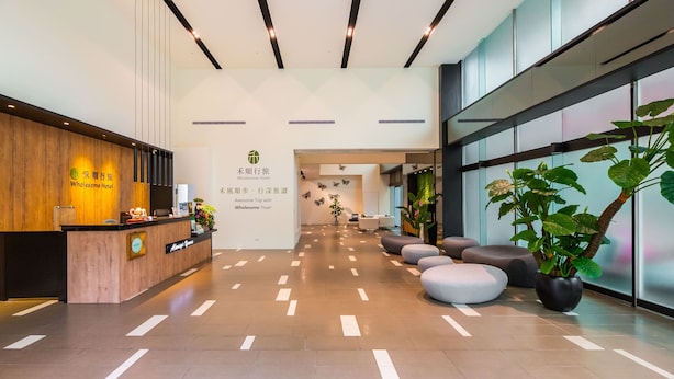 A hotel reception area with a wooden reception desk, a sign reading "Wholesome Hotel," and a modern interior design with a tiled floor and seating area. - Wholesome Hotel  (Taipei)