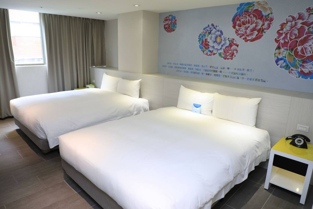 A hotel room with two beds, a nightstand, and a wall with floral artwork.