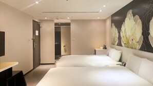 A hotel room with two beds, a desk, a chair, a small table with a coffee maker, and a wall with a floral painting. - Wholesome Hotel  (Taipei)