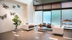 A modern lobby with two white sofas, a glass coffee table, decorative butterflies on the wall, and a potted plant. - Wholesome Hotel  (Taipei)