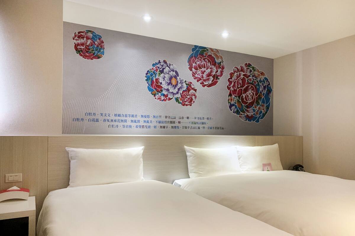 A hotel room with two beds, a wooden headboard, and a wall with floral artwork.
