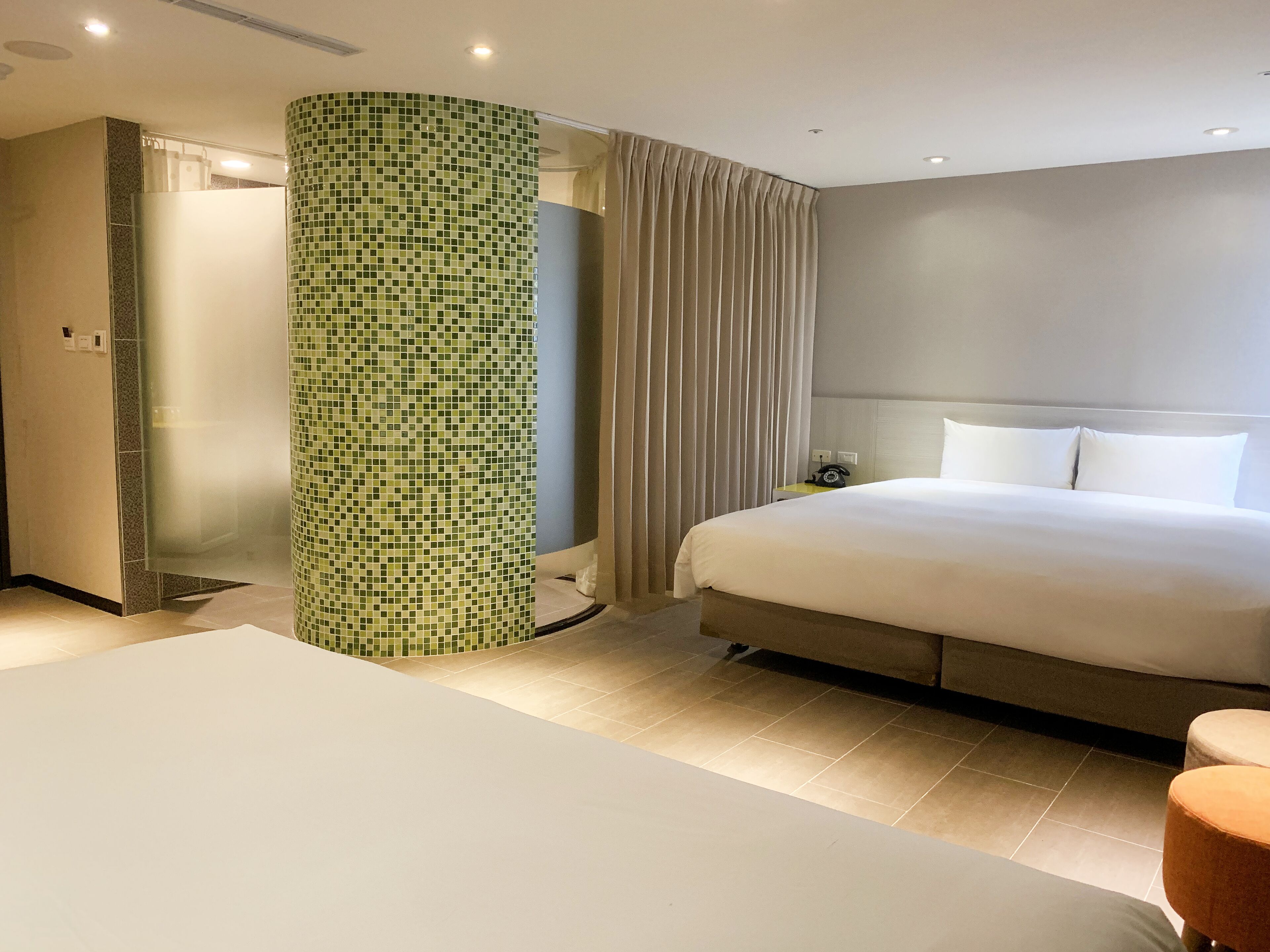 Ein Hotelzimmer mit einem großen Bett, einem Badezimmer mit einer grunen Mosaikwand und einem Vorhang.
