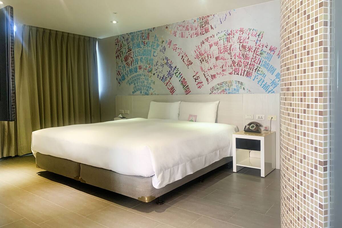 A hotel room with a large bed, a bedside table with a lamp, and a wall with colorful text.