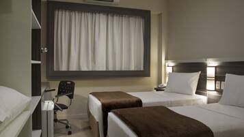 Habitación de hotel con dos camas, un escritorio con silla, aire acondicionado y una ventana con cortinas.