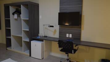 A modern room with a built-in wardrobe, a desk with a chair, a flat-screen TV, and a small refrigerator.