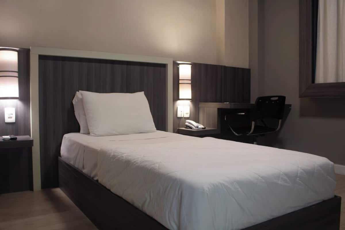 Una habitación de hotel con una cama grande, lámparas de noche, un escritorio con silla y un teléfono.