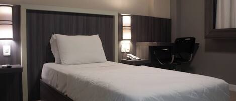 A hotel room with a large bed, bedside lamps, a desk with a chair, and a telephone.