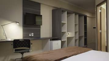 Habitació d'hotel amb llit, escriptori amb ordinador, cadira, televisió penjada a la paret i prestatges integrats.
