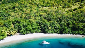 A boat on a clear turquoise beach surrounded by dense green forest. - Tet Rouge Resort St. Lucia (Choiseul)