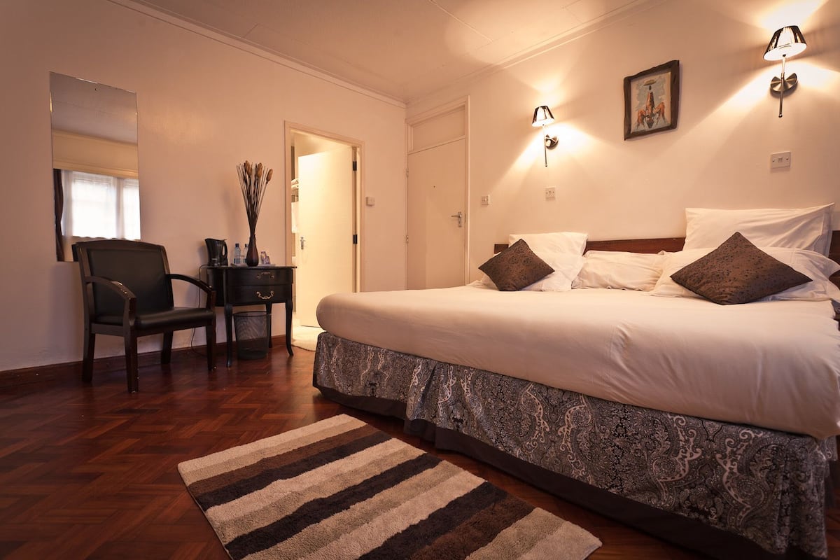 Un dormitorio con cama, lámparas de noche, una silla, un escritorio y una puerta.