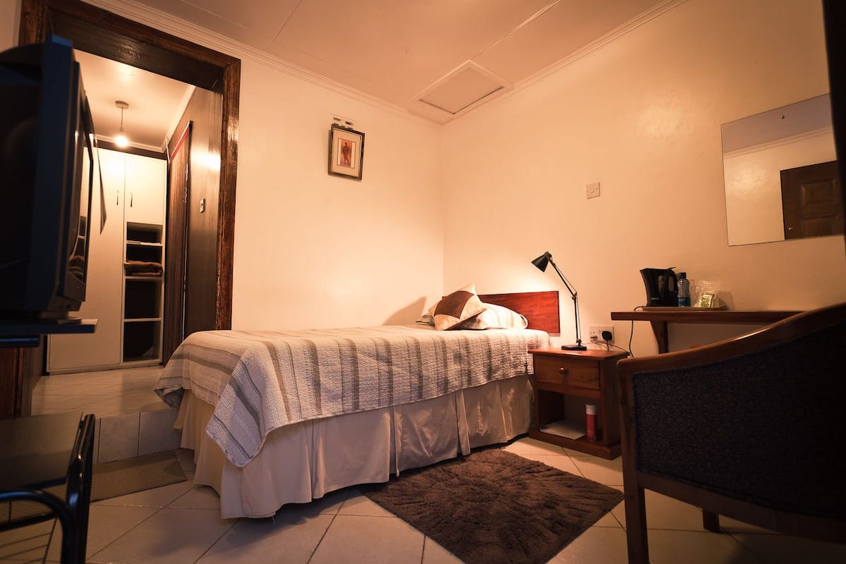 Habitación de hotel con cama, mesita de noche, lámpara, silla y un pequeño escritorio con espejo.