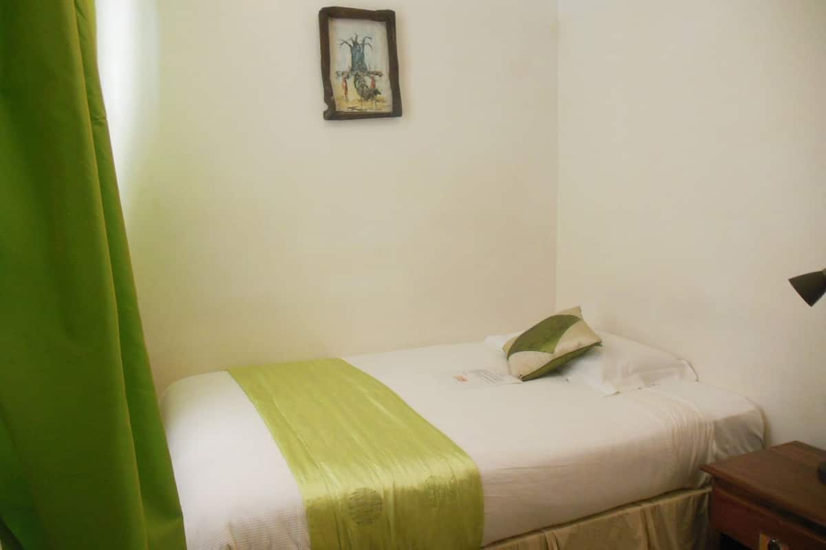 Una cama individual con una colcha verde, una almohada y una mesita de noche con una lámpara.