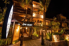 A building with a sign reading 'FEI SURF' at the entrance, surrounded by palm trees and stone statues. - 墾丁阿飛衝浪旅店 Afei Surf Inn - 步行南灣五分鐘 5 Min Walk from South Beach (Hengchun)