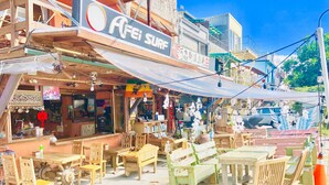 Ein Straßencafé mit Holztischen und -stühlen, einem Schild mit der Aufschrift 'AFEI SURF' und Blick auf die Straße.