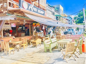 An outdoor cafe with wooden tables and chairs, a sign for 'AFEI SURF', and a view of the street. - 墾丁阿飛衝浪旅店 Afei Surf Inn - 步行南灣五分鐘 5 Min Walk from South Beach (Hengchun)