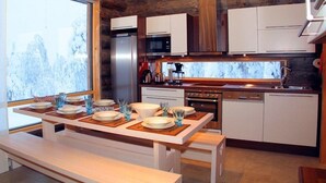 Une cuisine moderne avec des meubles blancs, des appareils en acier inoxydable et une table à manger en bois pour quatre personnes.